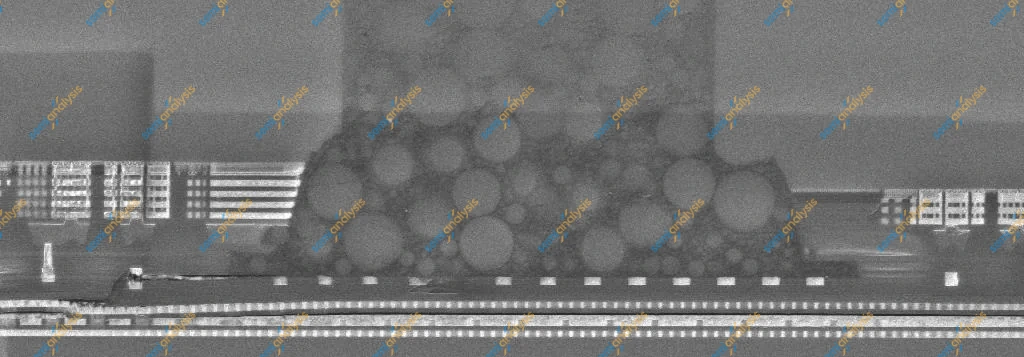 Grey electron-microscope image of a cross-section, a cluster of round filler particles beside stacked metal layers