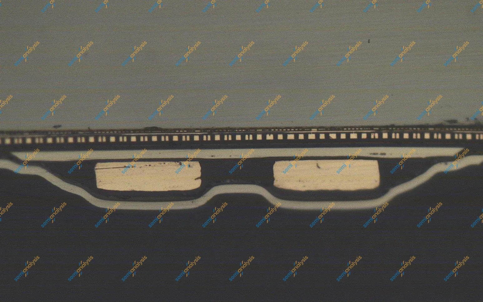 Polished cross-section of a small chip on a circuit board, two pale copper features under a thin die on a dark background